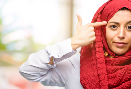 Young arab woman wearing hijab unhappy making suicide gesture, tired of everything. Shoots with his hand imitating gun, upsetの写真素材