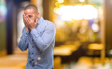 African american man with beard smiling having shy look peeking through fingers, covering face with hands looking confusedly broadly at nightの写真素材