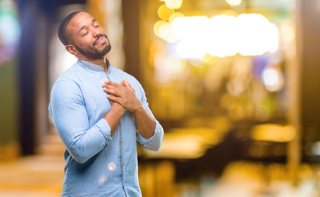 African american man with beard with hands in heart, expressing love and health concept at nightの写真素材