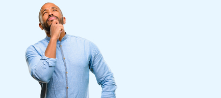 African american man with beard thinking and looking up expressing doubt and wonder isolated over blue backgroundの写真素材