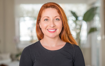 Redhead woman at home with a happy face standing and smiling with a confident smile showing teeth
