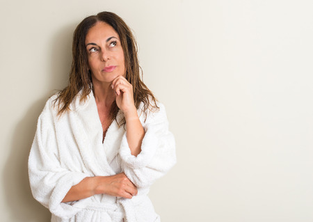 Beautiful middle age woman, wet hair wearing a towel serious face thinking about question, very...