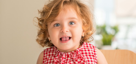 Beautiful blonde child with blue eyes smiling with tongue out at home.