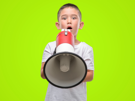 Dark haired little child holding megaphone scared in shock with a surprise face, afraid and excited with fear expressionの写真素材
