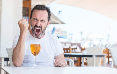 Handsome senior man drinking beer at restaurant annoyed and frustrated shouting with anger, crazy and yelling with raised hand, anger conceptの写真素材