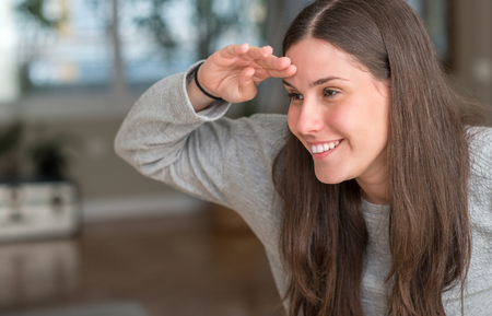 Young beautiful woman at home very happy and smiling looking far away with hand over head. Searching concept.の写真素材