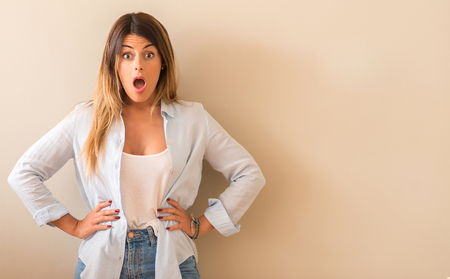 Young beautiful woman wearing a shirt with surprised face leaning on the wall at home.の写真素材