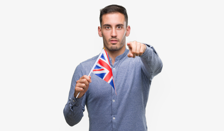 Handsome young man holding a flag of United Kingdom pointing with finger to the camera and to you, hand sign, positive and confident gesture from the frontの写真素材