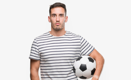 Handsome young man holding soccer football with a confident expression on smart face thinking seriousの写真素材