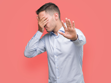 Handsome young businessman covering eyes with hands and doing stop gesture with sad and fear expression. Embarrassed and negative concept.の写真素材