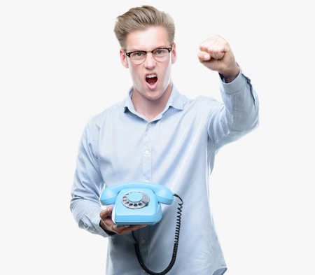 Young handsome blond man holding vintage telephone annoyed and frustrated shouting with anger, crazy and yelling with raised hand, anger conceptの写真素材