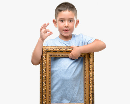 Dark haired little child holding frame doing ok sign with fingers, excellent symbolの写真素材