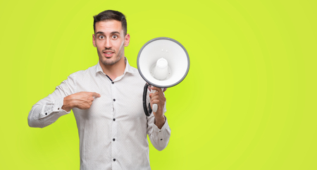 Handsome young man holding microphone with surprise face pointing finger to himselfの写真素材
