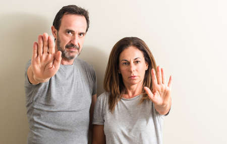 Middle age couple, woman and man with open hand doing stop sign with serious and confident...