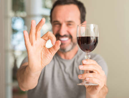 Middle age man drinking a glass of wine doing ok sign with fingers, excellent symbolの写真素材