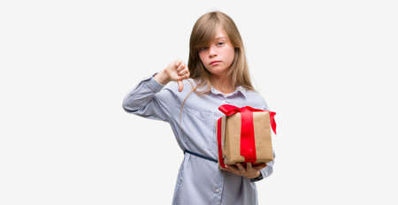 Young blonde toddler holding a present with angry face, negative sign showing dislike with thumbs down, rejection conceptの写真素材
