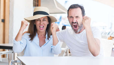 Middle age couple sitting at terrace annoyed and frustrated shouting with anger, crazy and yelling with raised hand, anger conceptの写真素材