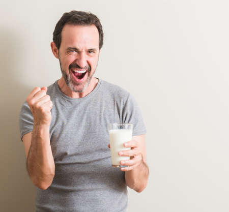 Senior man drinking a glass of milk screaming proud and celebrating victory and success very excited, cheering emotionの写真素材