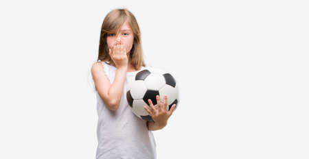Young blonde toddler holding football ball cover mouth with hand shocked with shame for mistake,...