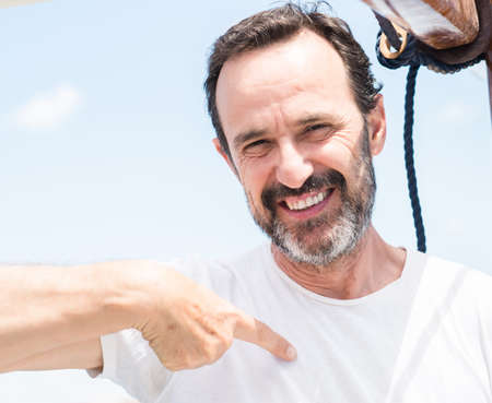 Handsome senior man traveling on sailboat with surprise face pointing finger to himself