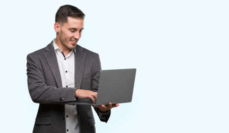Handsome young man using computer laptop with a happy face standing and smiling with a confident smile showing teethの写真素材