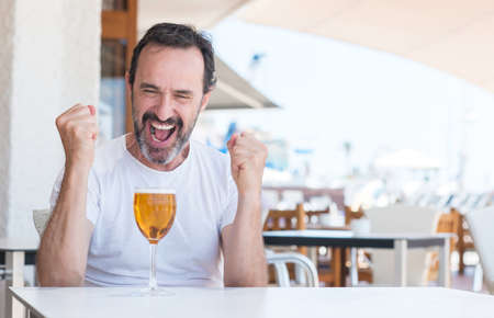 Handsome senior man drinking beer at restaurant screaming proud and celebrating victory and success very excited, cheering emotionの写真素材