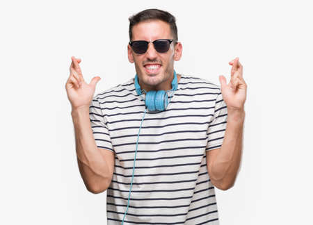 Handsome young man wearing headphones smiling crossing fingers with hope and eyes closed. Luck and superstitious concept.の写真素材