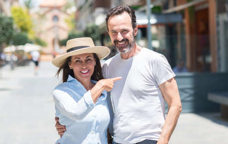 Middle age couple down the street very happy pointing with hand and finger