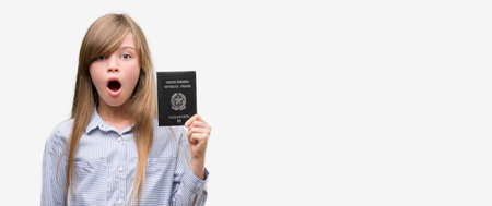 Young blonde toddler holding italian passport scared in shock with a surprise face, afraid and...