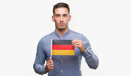 Handsome young man holding a flag of Germany with a confident expression on smart face thinking seriousの写真素材