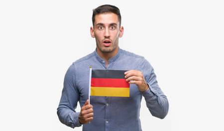 Handsome young man holding a flag of Germany scared in shock with a surprise face, afraid and excited with fear expressionの写真素材