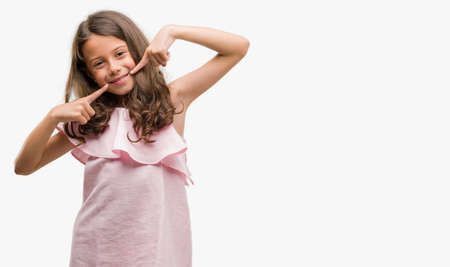 Brunette hispanic girl wearing pink dress smiling confident showing and pointing with fingers teeth...