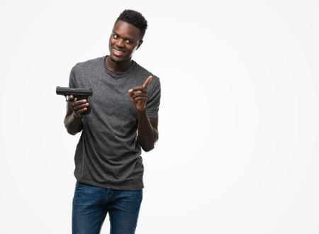 Young african american man holding a gun very happy pointing with hand and finger to the sideの写真素材