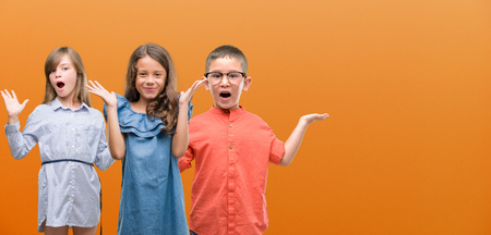 Group of boy and girls kids over orange background very happy and excited, winner expression...