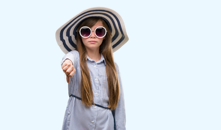 Young blonde toddler wearing hat and sunglasses with angry face, negative sign showing dislike with thumbs down, rejection conceptの写真素材