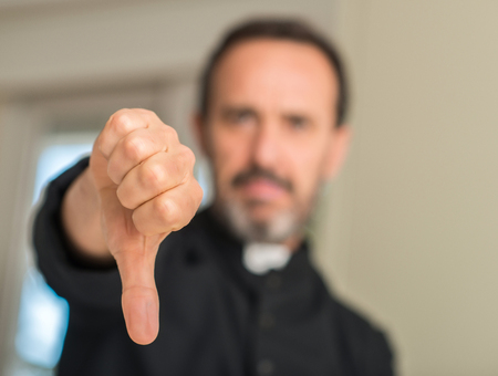 Christian priest man with angry face, negative sign showing dislike with thumbs down, rejection conceptの写真素材