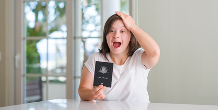 Down syndrome woman at home holding australian passport stressed with hand on head, shocked with shame and surprise face, angry and frustrated. Fear and upset for mistake.の写真素材