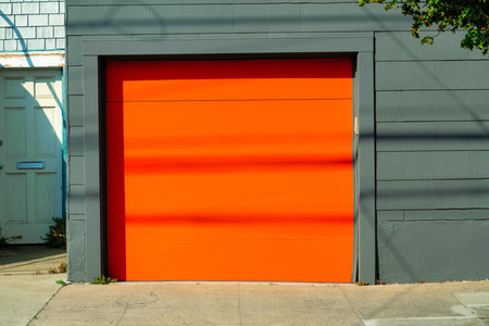 Orange garage door on green gray colored timber wood frame house background with blue slatted wood house nearby at home in the neighborhoodの写真素材
