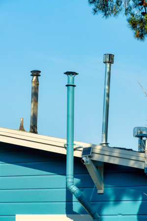 Metal chimney pipe on stucco gray and white exterior of house or home in shade and partial sun in late afternoon in the suburbs. In the urban neighborhood with blue sky background in the city.の写真素材