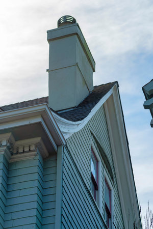 Modern home exterior or facade with victorian accents and decorations and tall chimney with blue and white gradient sky in the front yard. In the city or neighborhood in suburban area.の写真素材