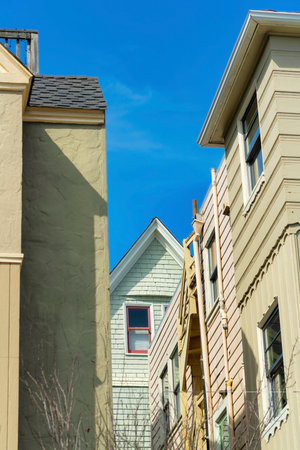 Metal fire escape balcony with rooftop access ladder on red stucco building with brown roof tiles on facade front of building. Blue sky background in midday sun in the city or urban area downtown.の写真素材