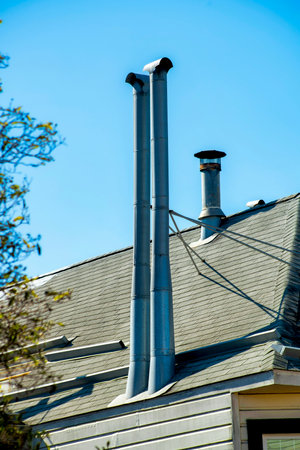 Close view of gray metal chimney pipes in sunset or twilight sun on side of building with wooden facade and blue sky background. In the city or in an urban area of the town downtown.の写真素材
