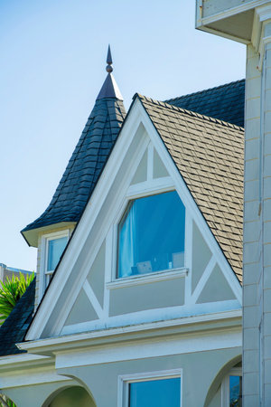 Brown beige stucco building with barn style roof and light tiles with victorian window decoration and front yard trees in late afternoon shade and sun. In the neighborhood or in the city suburbs.の写真素材