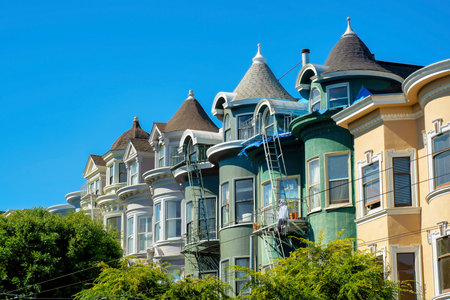 Row of modern house facades beige and green in late afternoon shade and blue and white gradient sky background. In the downtown neighborhood in historic districts of San Francisco California.の写真素材