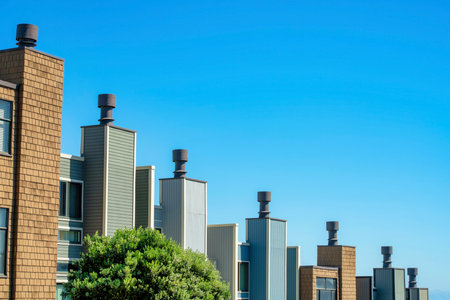 Decorative chimneys in row in neighborhood with wooden slats or panels with metal tops and gradient blue and white sky background. In the city in the suburban areas with front yard green trees.の写真素材
