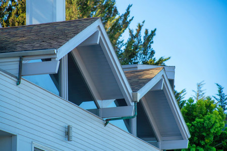 Double gable style a frame roofs with window walls and white stucco house with back yard trees and blue gradient sky background. In late afternoon shade in the suburban part of the neighborhood.の写真素材