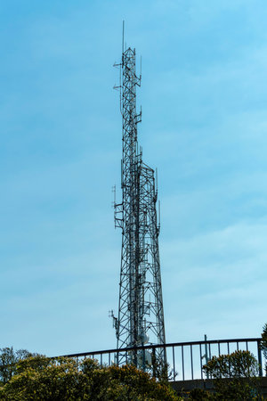 metal radio tower with antenas and pipes in shade with public view area foreground with whispy white and blue cloudy skyの写真素材