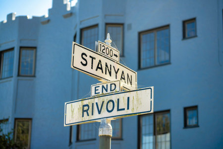Road sign that says Sanyan and Rivoli with white and black paint on streets with suburban or uban building in background. In shade with small blue sky background in the downtown city or neighborhood.の写真素材