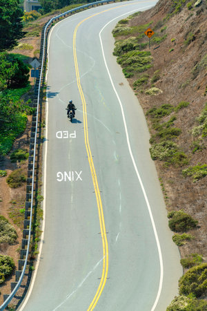 lone biker dressed in black on curvy moutain road with gaurd rails and trees and foliage in sunlight late afternoon in canyonの写真素材