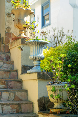 Front porch or stoop with stoic style vases or potted plants on ledges near stone steps with...